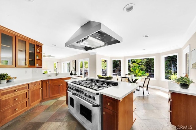 kitchen featuring wall chimney range hood, range with two ovens, light countertops, and brown cabinetry