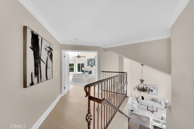 hallway with a notable chandelier, baseboards, wood finished floors, and an upstairs landing