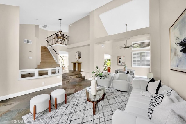 living room featuring stairs, visible vents, a towering ceiling, baseboards, and ceiling fan with notable chandelier