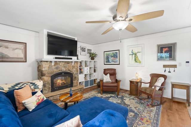 living room featuring ceiling fan, a stone fireplace, wood finished floors, and baseboards