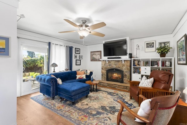 living area with ceiling fan, a stone fireplace, and wood finished floors