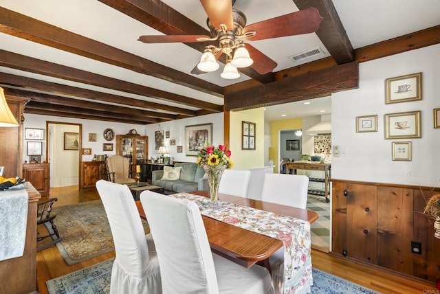 dining space featuring visible vents, wainscoting, ceiling fan, wood finished floors, and beam ceiling