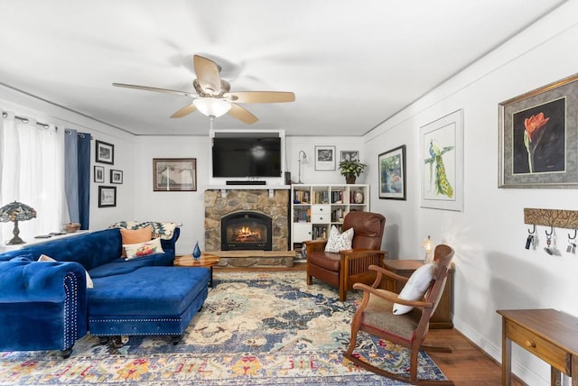 living room with baseboards, a ceiling fan, wood finished floors, and a stone fireplace