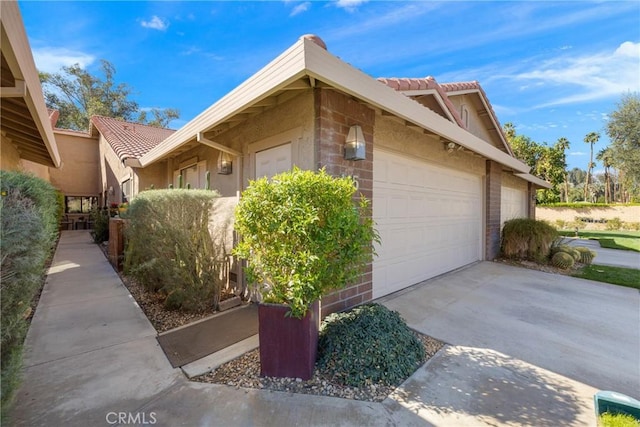 view of side of property featuring a garage, a tiled roof, concrete driveway, and stucco siding