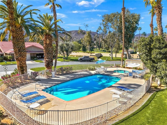 view of pool featuring a community hot tub, a yard, fence, and a mountain view