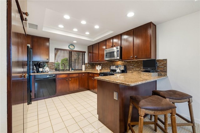 kitchen with range with gas stovetop, dishwasher, stainless steel microwave, a peninsula, and a tray ceiling