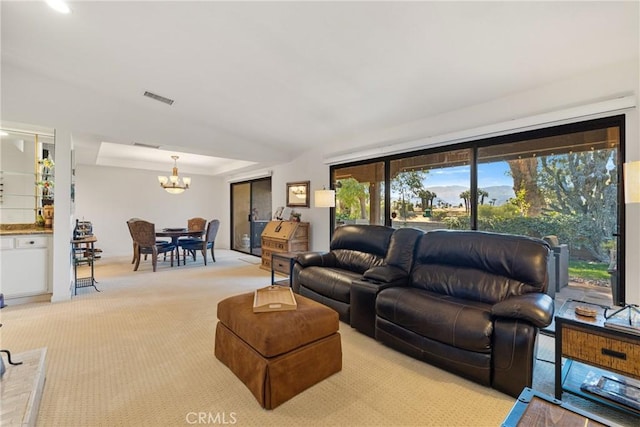 living room featuring light carpet, visible vents, a raised ceiling, and a notable chandelier