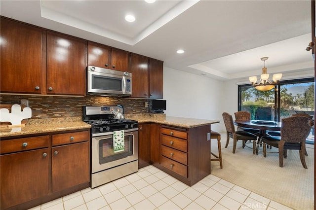 kitchen with light stone counters, a tray ceiling, decorative backsplash, appliances with stainless steel finishes, and a peninsula