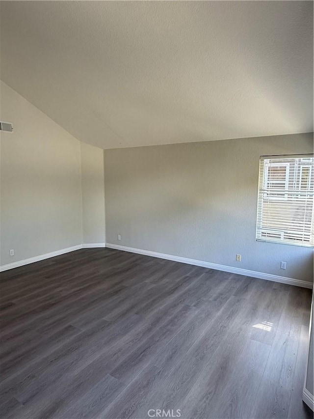 unfurnished room featuring lofted ceiling, dark wood-type flooring, a textured ceiling, and baseboards