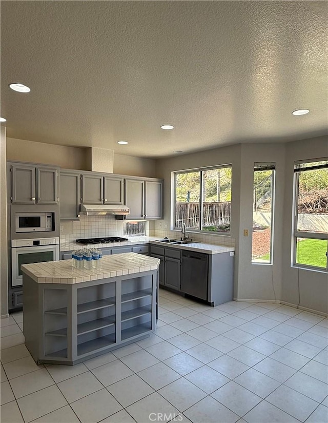 kitchen with under cabinet range hood, white appliances, gray cabinets, tile counters, and open shelves