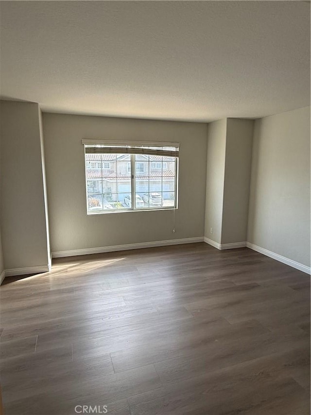 spare room featuring a textured ceiling, baseboards, and wood finished floors