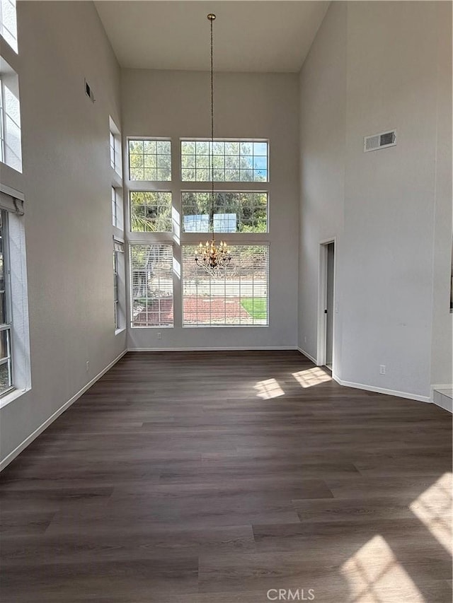 unfurnished dining area with a chandelier, a high ceiling, dark wood-type flooring, and visible vents