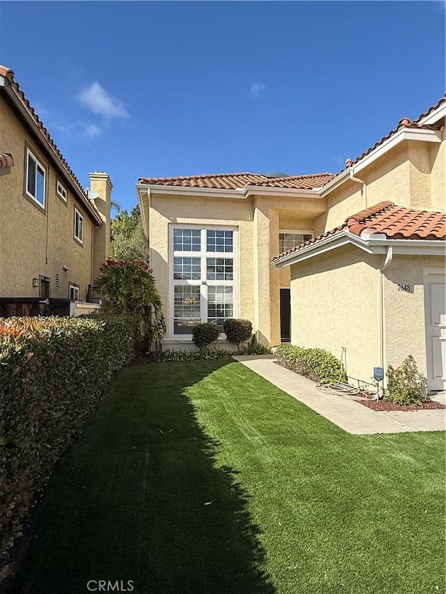 exterior space with a tile roof, a lawn, and stucco siding