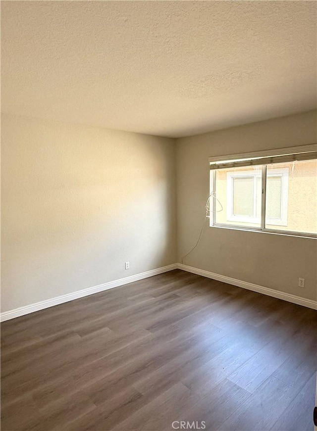 spare room with dark wood-style floors, a textured ceiling, and baseboards