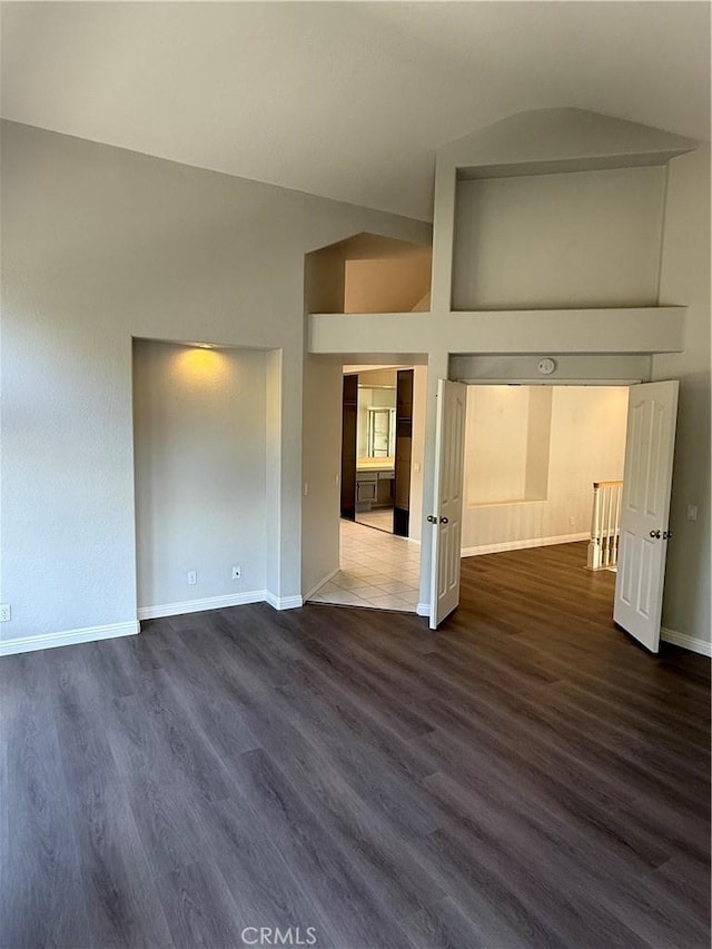 spare room with dark wood-style floors, baseboards, and high vaulted ceiling