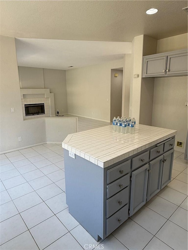 kitchen with open floor plan, light tile patterned floors, a tile fireplace, and gray cabinets