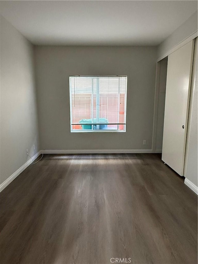 unfurnished bedroom with a closet, dark wood finished floors, and baseboards