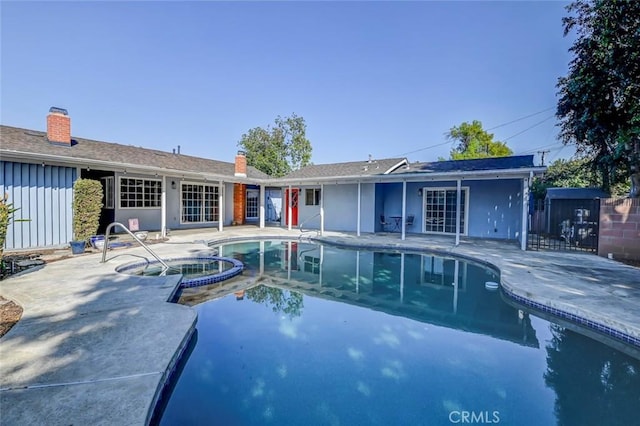 back of house featuring a patio, board and batten siding, fence, and a pool with connected hot tub