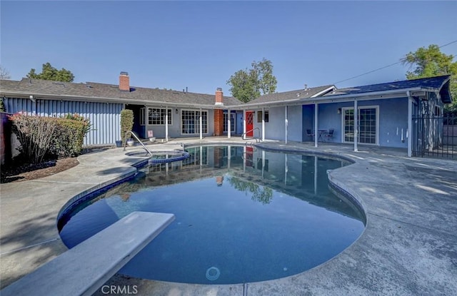 view of pool with a patio, fence, french doors, a pool with connected hot tub, and a diving board