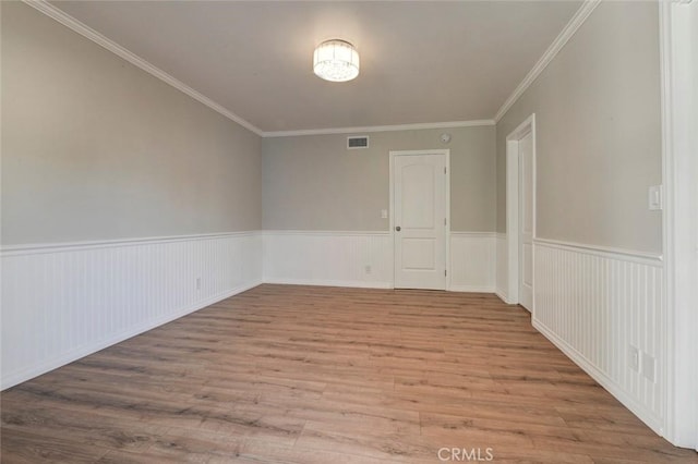 empty room with a wainscoted wall, ornamental molding, wood finished floors, and visible vents