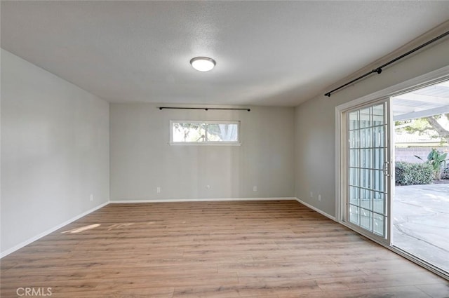 empty room featuring light wood-type flooring, a textured ceiling, and baseboards