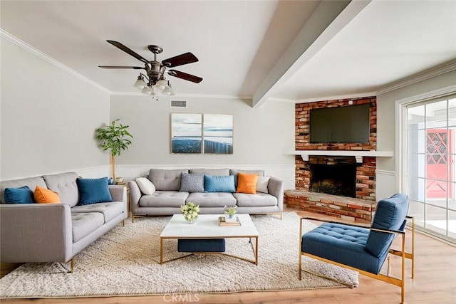 living room featuring visible vents, ornamental molding, wood finished floors, beamed ceiling, and a brick fireplace