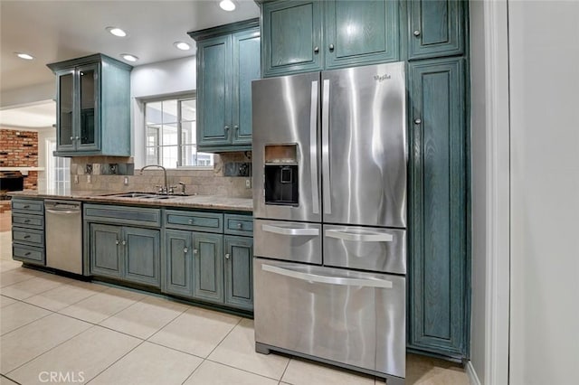 kitchen featuring stone countertops, light tile patterned flooring, a sink, appliances with stainless steel finishes, and decorative backsplash