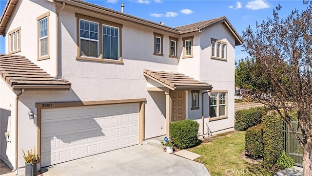 view of front facade with an attached garage, a tile roof, concrete driveway, and stucco siding