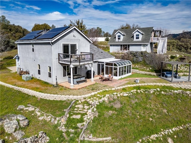 rear view of house featuring stucco siding, solar panels, a sunroom, a patio area, and a jacuzzi