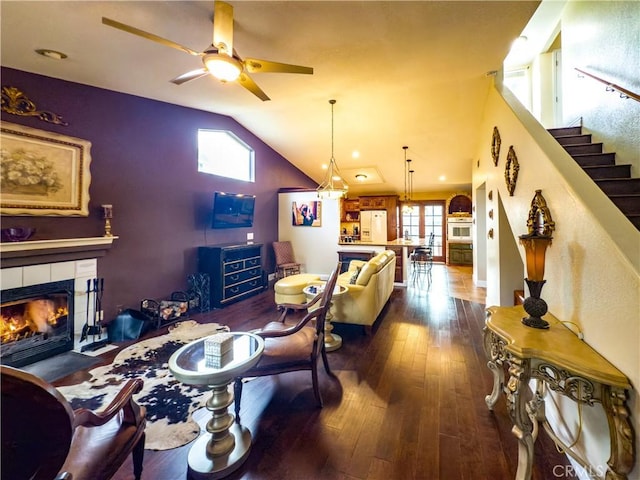 living area with a tile fireplace, lofted ceiling, wood-type flooring, ceiling fan, and stairway