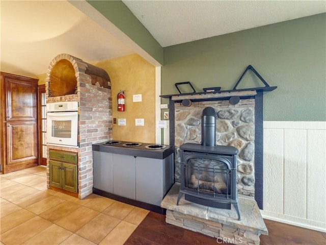 kitchen with light tile patterned floors, electric cooktop, white oven, brown cabinets, and a wood stove