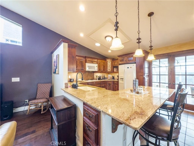 kitchen with a breakfast bar, vaulted ceiling, a sink, white appliances, and a peninsula