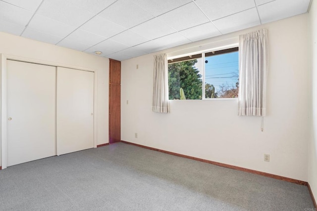 unfurnished bedroom with a closet, carpet flooring, a paneled ceiling, and baseboards