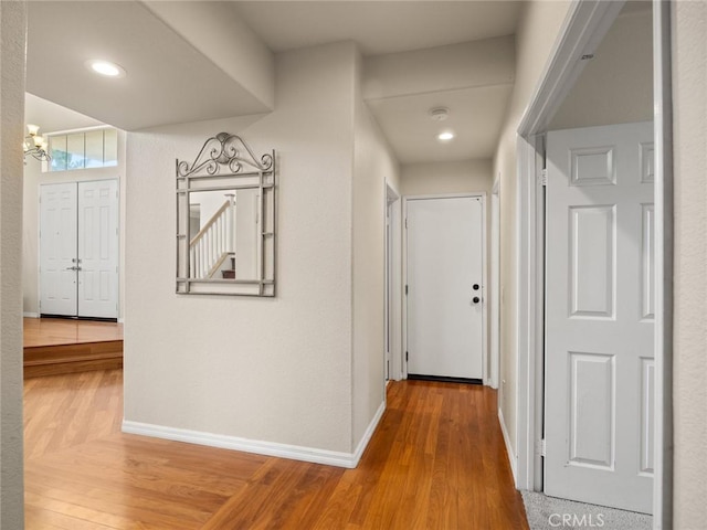 hall featuring a notable chandelier, baseboards, and wood finished floors