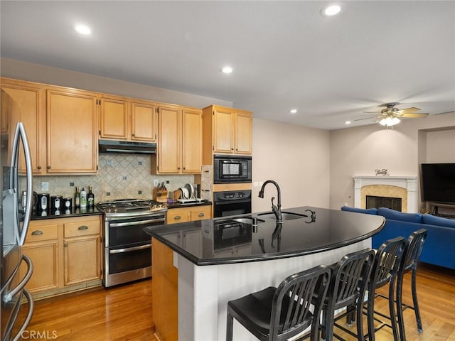 kitchen with open floor plan, a sink, light wood-type flooring, under cabinet range hood, and black appliances