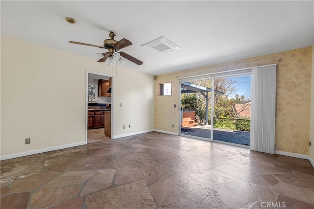 spare room featuring stone finish floor, visible vents, baseboards, and wallpapered walls