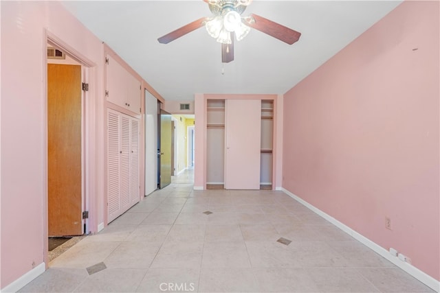 unfurnished bedroom with two closets, light tile patterned floors, visible vents, a ceiling fan, and baseboards