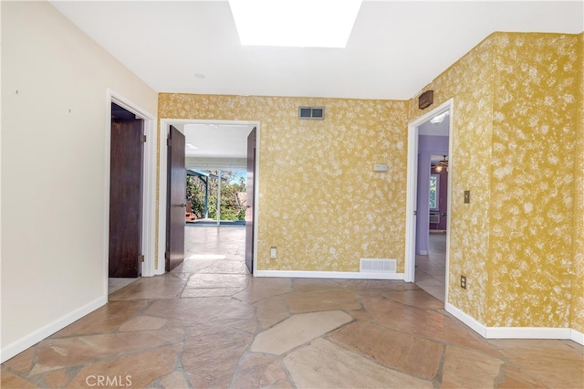 spare room featuring wallpapered walls, baseboards, a skylight, and visible vents