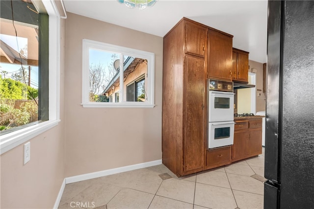 kitchen with double oven, brown cabinetry, under cabinet range hood, and light tile patterned floors