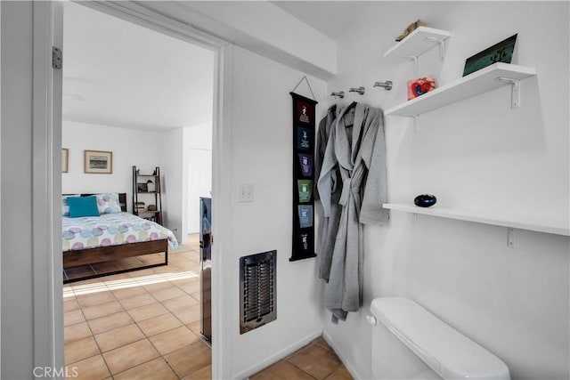 bathroom with toilet, heating unit, and tile patterned floors