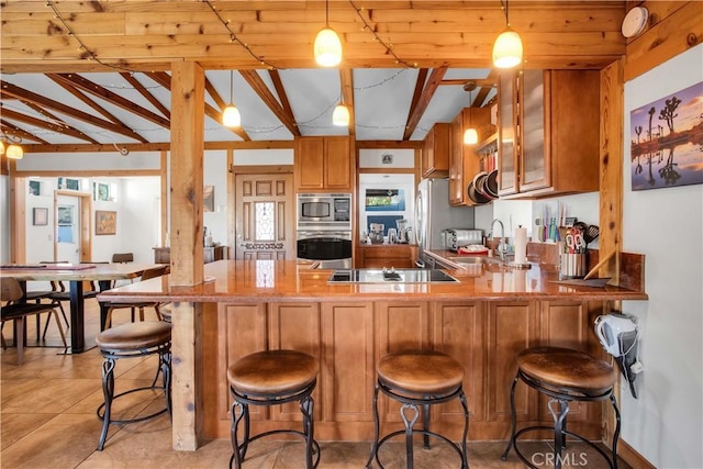 kitchen featuring a breakfast bar, brown cabinets, lofted ceiling with beams, appliances with stainless steel finishes, and a peninsula