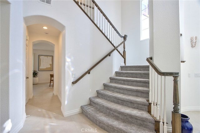 stairs with baseboards, visible vents, a high ceiling, arched walkways, and tile patterned floors