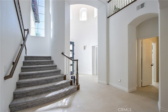 stairway with tile patterned floors, arched walkways, visible vents, and a towering ceiling