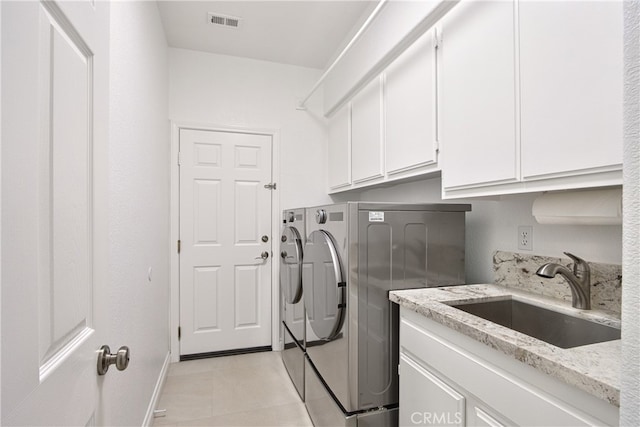 laundry area featuring light tile patterned floors, visible vents, washing machine and clothes dryer, cabinet space, and a sink