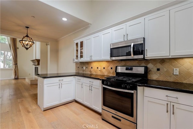 kitchen featuring decorative backsplash, appliances with stainless steel finishes, ornamental molding, a peninsula, and white cabinetry