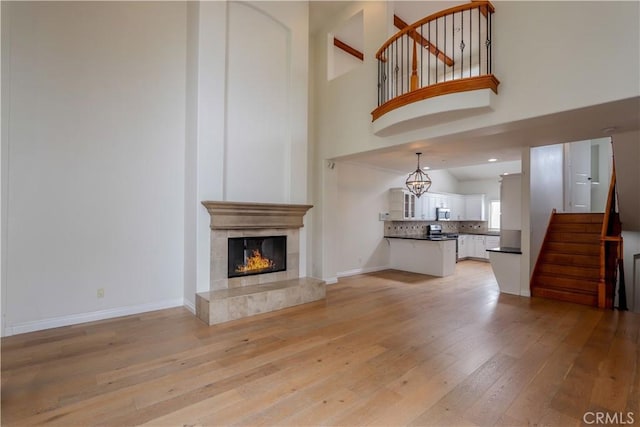 unfurnished living room featuring light wood finished floors, baseboards, a premium fireplace, and stairway