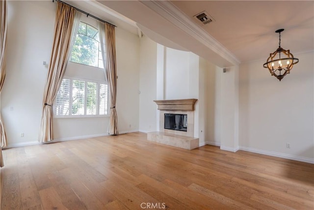 unfurnished living room with visible vents, a premium fireplace, ornamental molding, an inviting chandelier, and light wood-type flooring