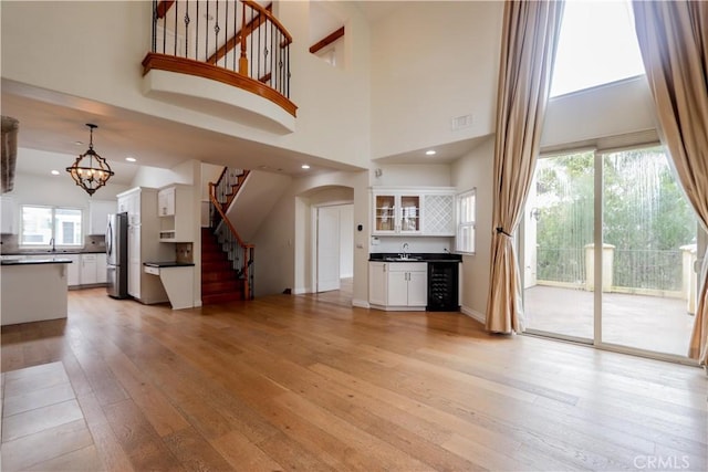 unfurnished living room featuring visible vents, stairway, an inviting chandelier, a sink, and light wood-type flooring