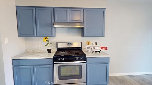 kitchen with under cabinet range hood, baseboards, light countertops, stainless steel gas stove, and light wood finished floors