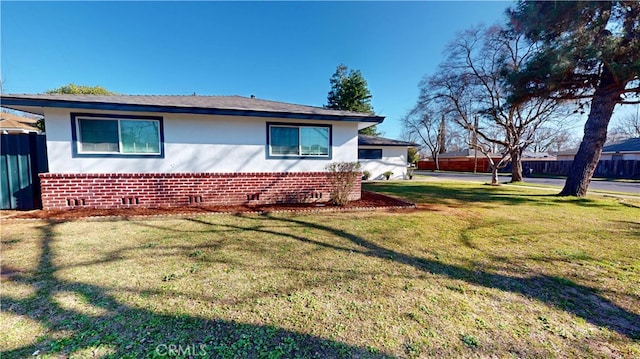 view of side of home featuring a yard, fence, and brick siding